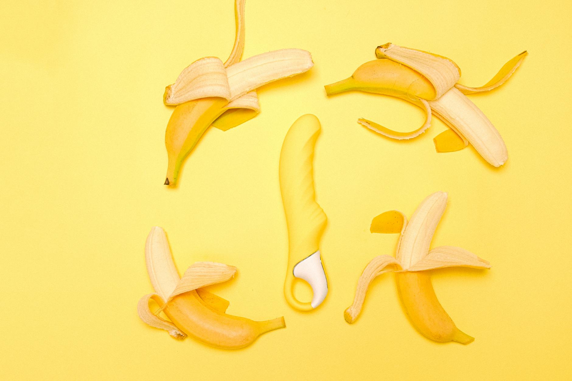 A yellow silicone lemon vibrator surrounded by peeled lemons on a yellow background