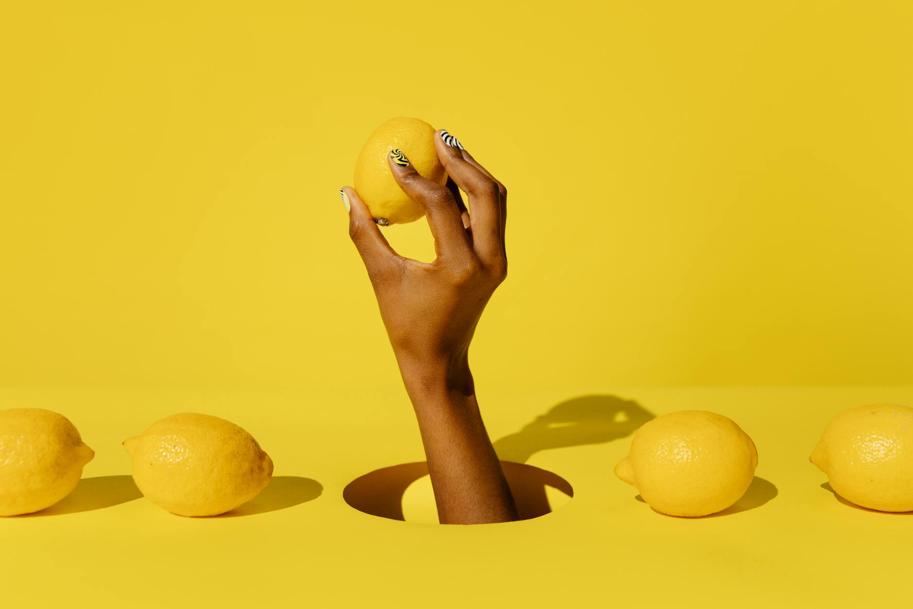 Hand holding a fresh lemon against a yellow background, symbolizing renewal and vitality