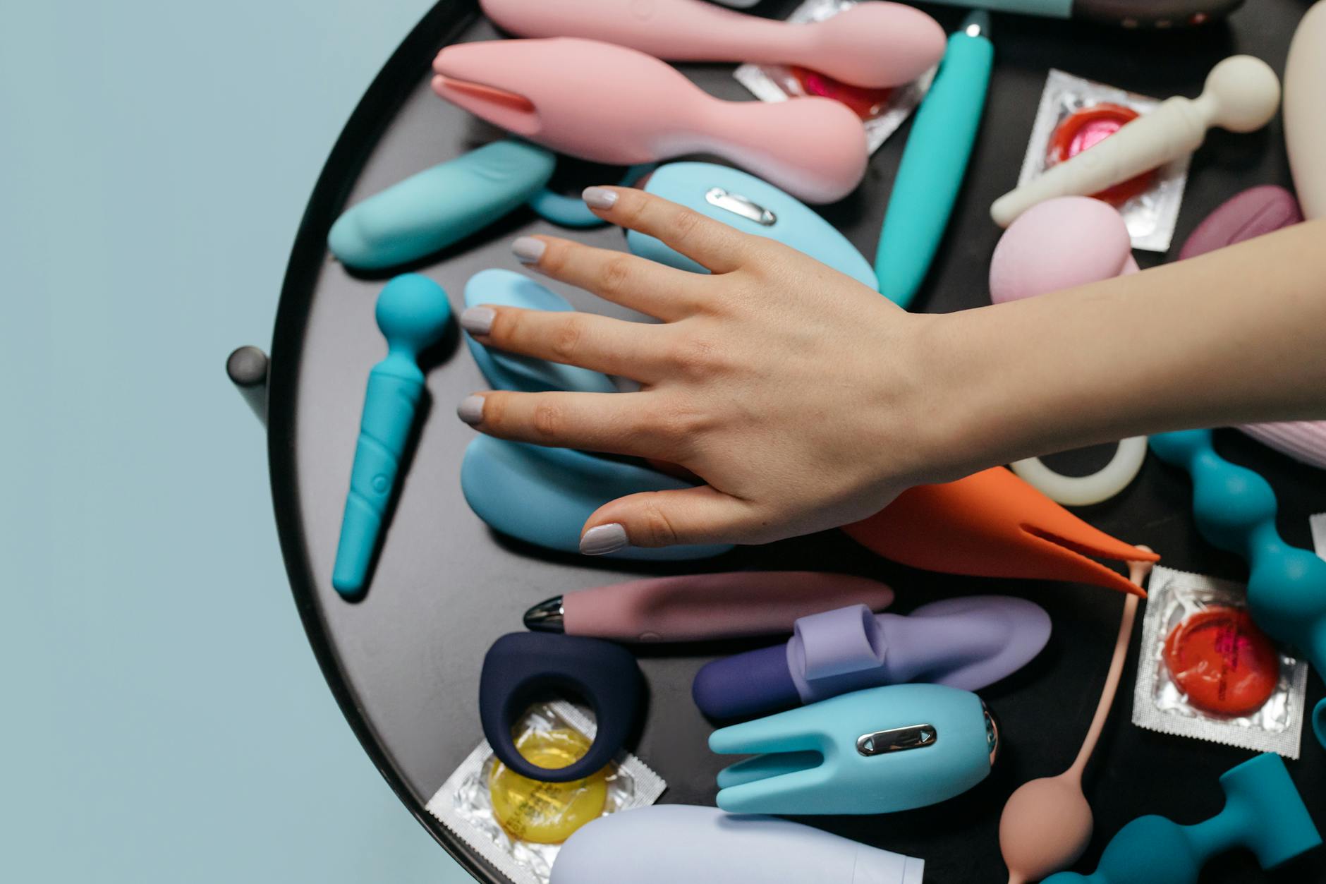Hand reaching toward a colorful lemon vibrator and other clitoral toys arranged thoughtfully on a surface.