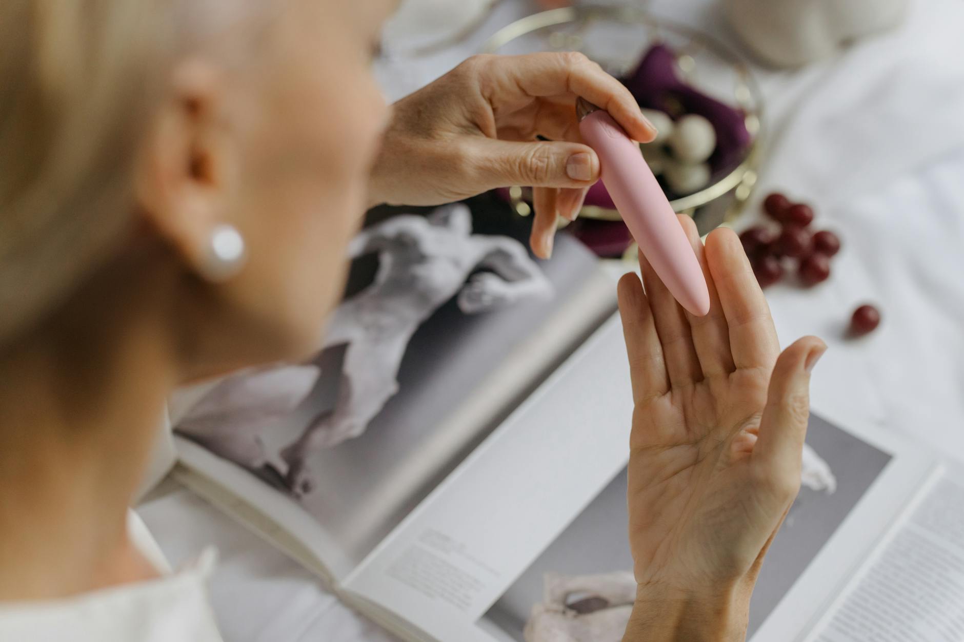 Woman holding a pink vibrator with art books, representing intimate reconnection and personal pleasure