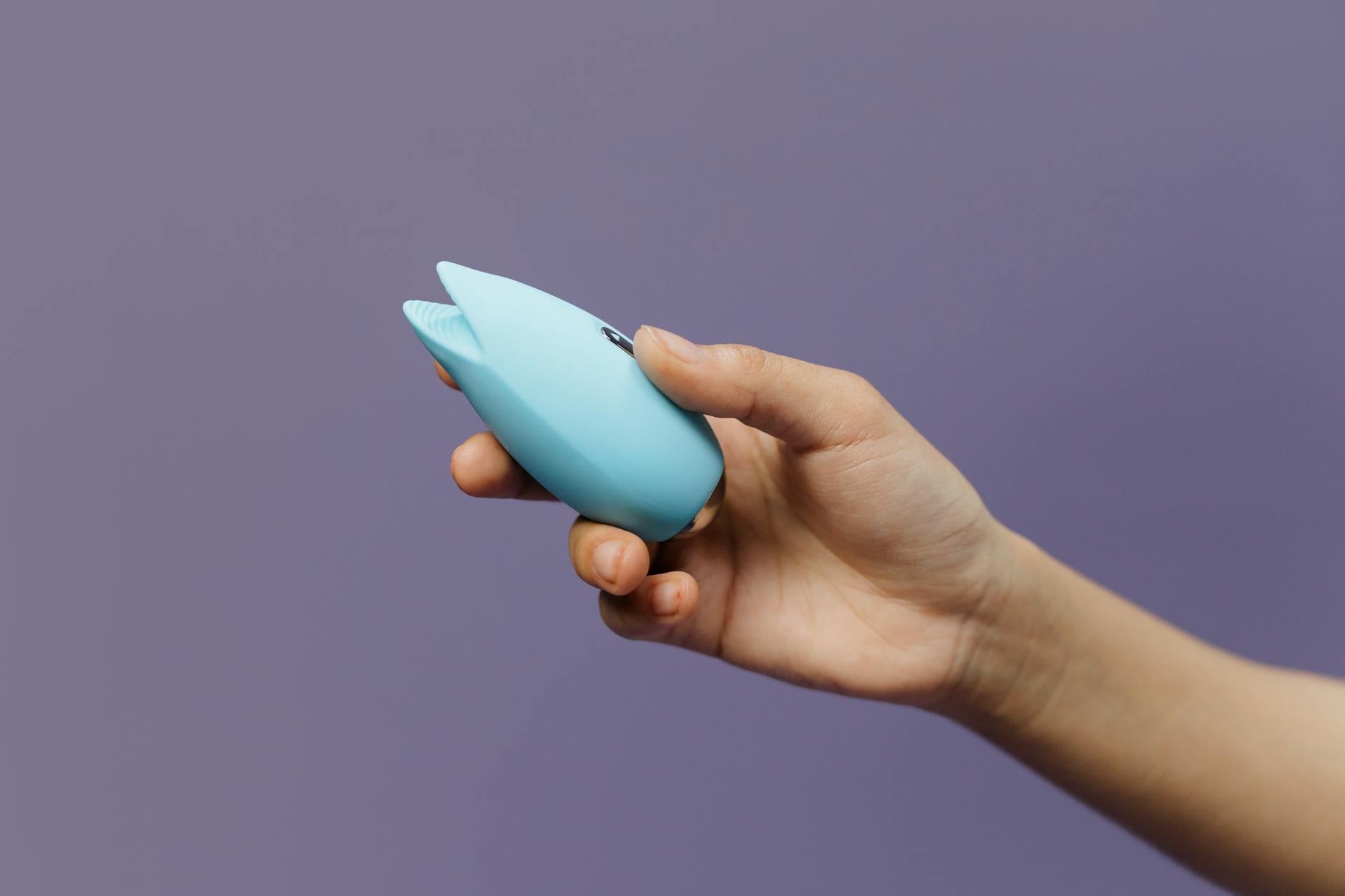 A blue silicone vibrator held in hand against a solid purple background, promoting self-love and intimacy