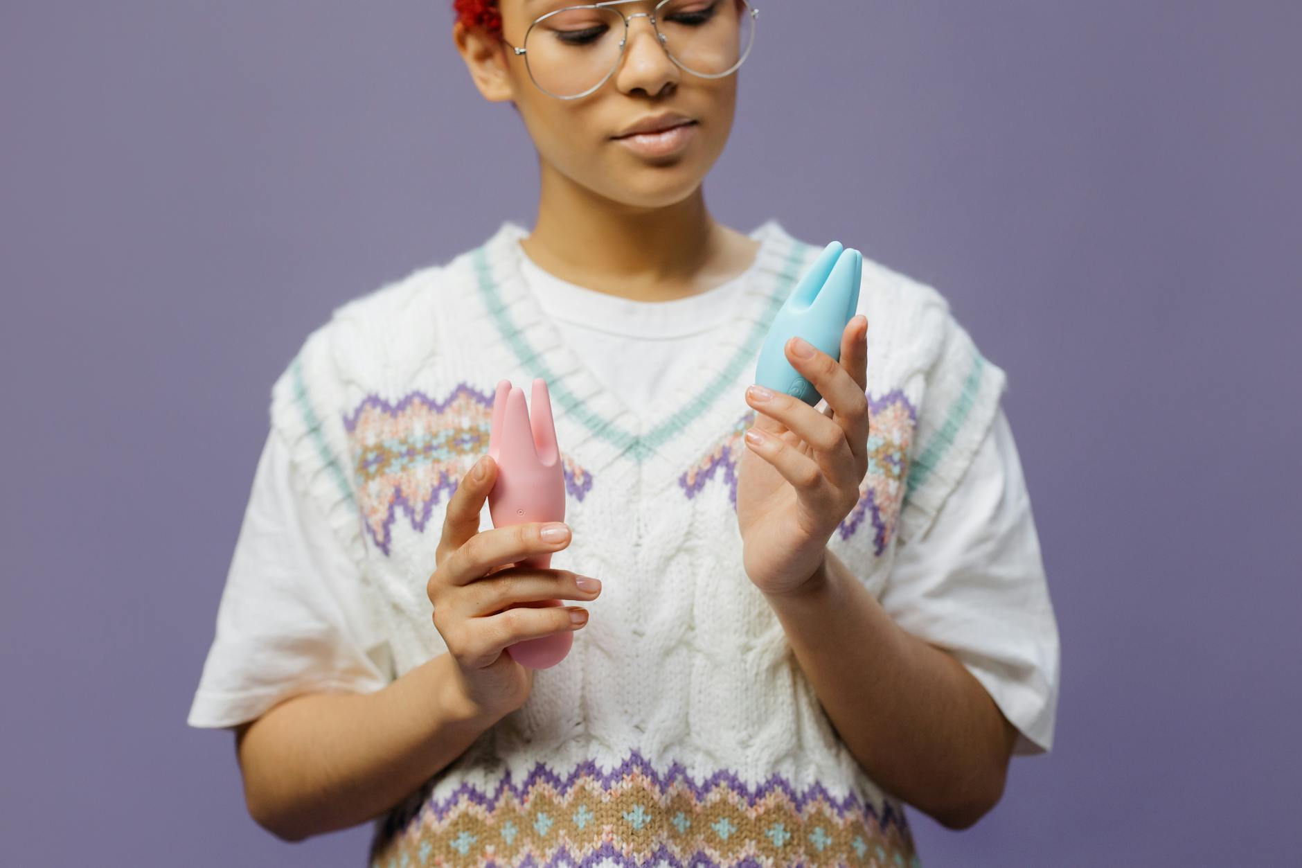 Woman holding blue and pink silicone vibrators in contemplative self-care moment