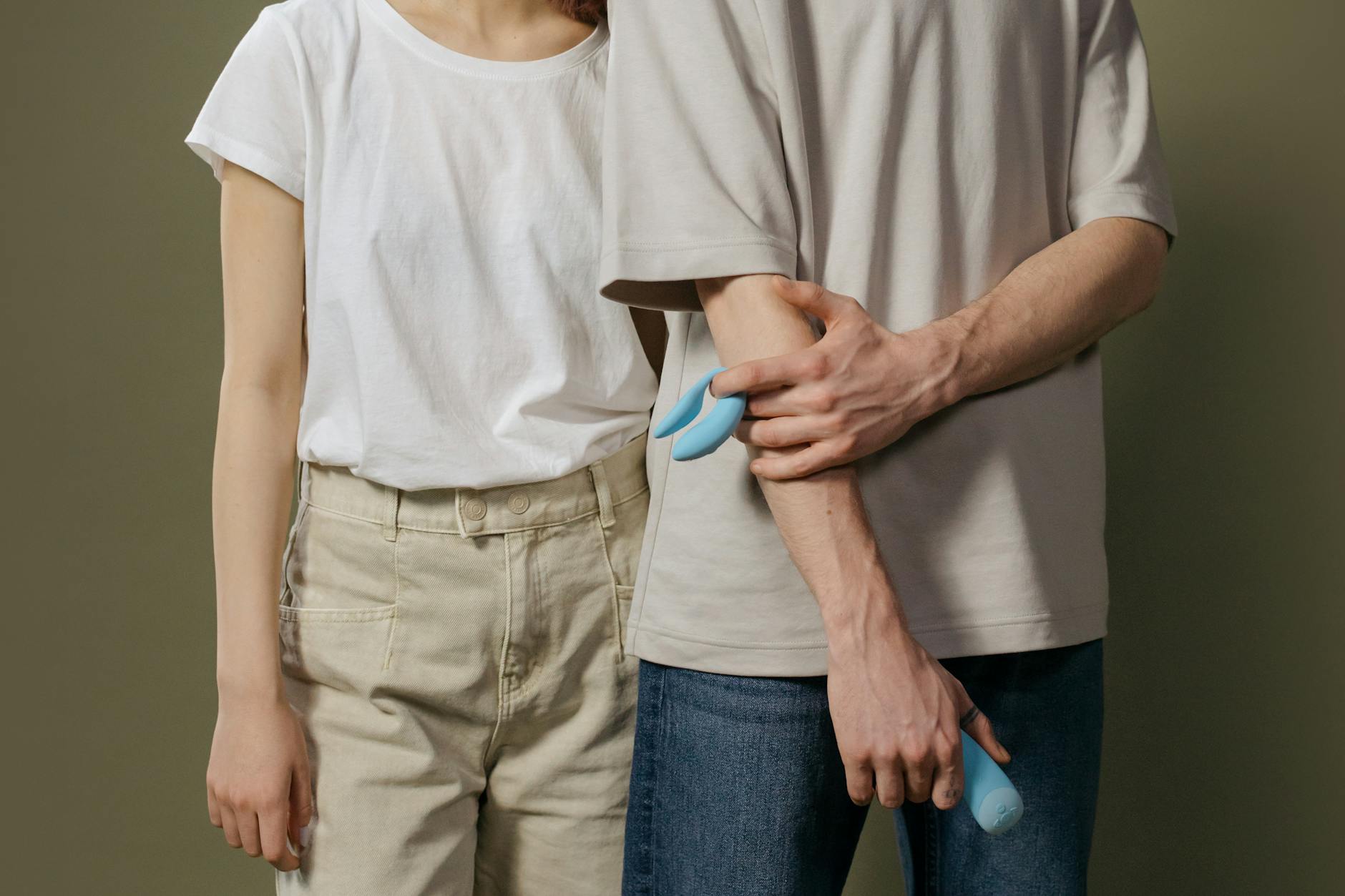 A hand holding a blue clitoral vibrator above a decorative glass bowl on a soft surface