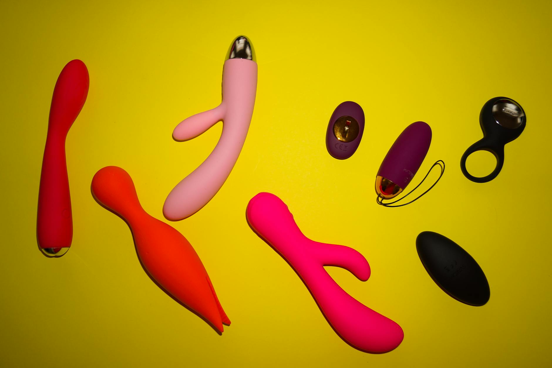 Close-up of a yellow lemon vibrator alongside other colorful adult toys on a bright yellow surface