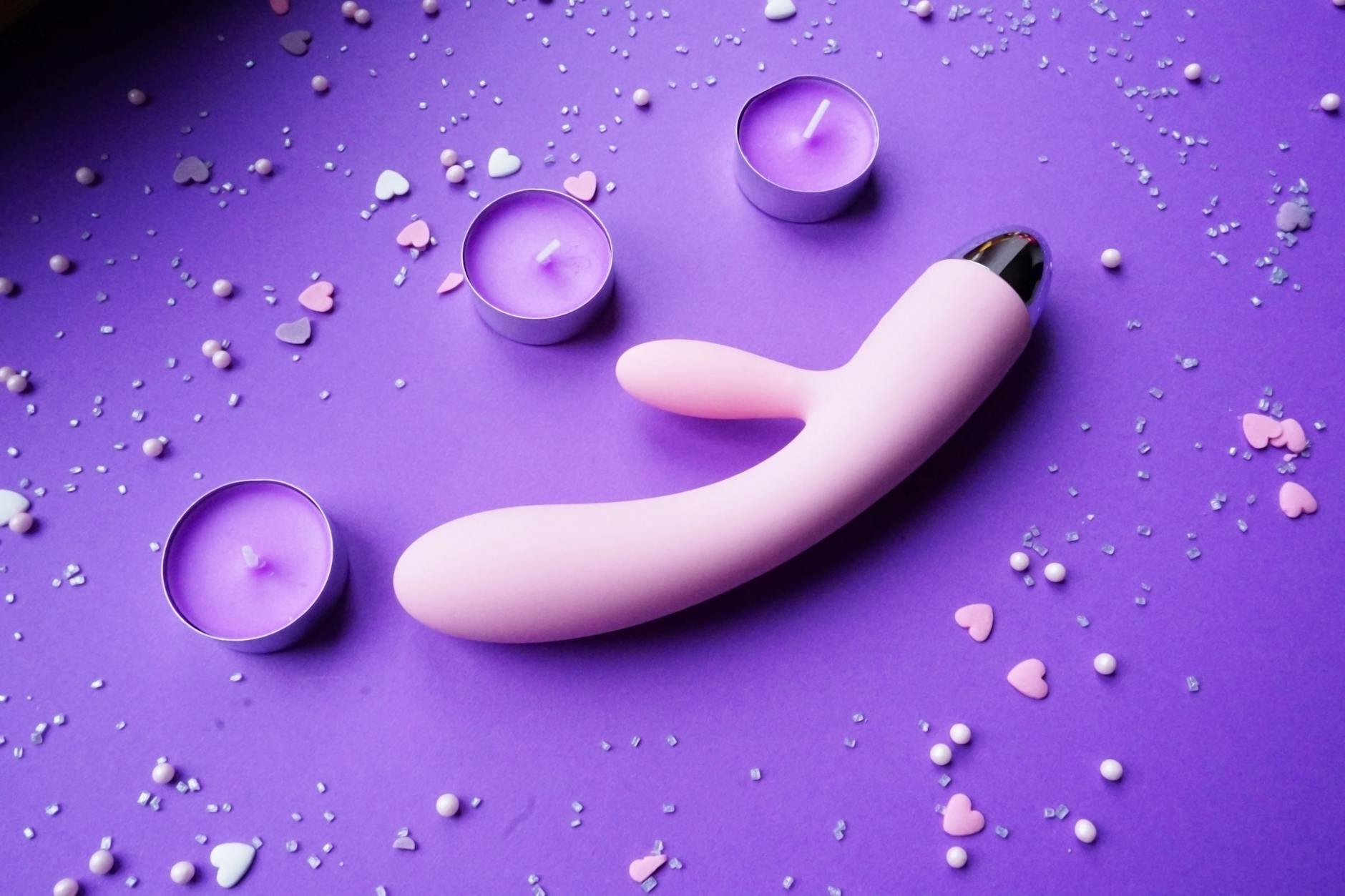 Pink vibrator surrounded by candles and heart confetti on purple background